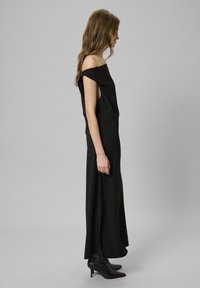 Robe maxi noire à épaules dénudées avec des fentes sur les côtés, réalisée en tissu lisse. Portée avec des bottines noires à bout pointu.