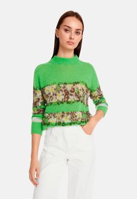 Grüner Strickpullover mit Stehkragen, verziert mit Tiermotiven und floralen Akzenten in horizontalen Streifen. Weiche Textur, Dreiviertelärmel.