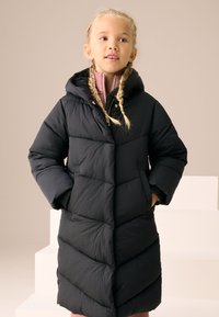 Doudoune noire avec capuche, dotée d'un design matelassé et de larges motifs en chevron. Équipée de poches latérales et d'une fermeture éclair.