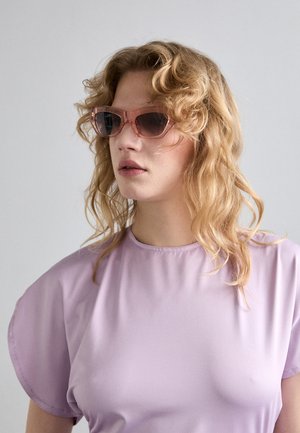 Pink tinted sunglasses with a geometric frame, paired with a soft lavender top featuring a round neckline and cap sleeves.