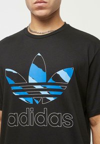 Fekete pamut póló, kék és fehér Adidas trefoil logó grafikával, textúrázott, kopott hatással.