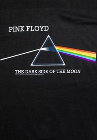 Svart T-skjorte med en trekantet prisme som har en hvit lysstråle og et regnbuespektrum; teksten leser "PINK FLOYD THE DARK SIDE OF THE MOON."