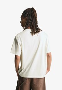 T-shirt oversize color crema realizzato in morbido cotone con maniche corte, presenta un piccolo logo nero sulla schiena vicino al colletto.