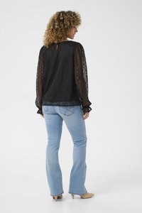 Black lace blouse with geometric patterns, long sleeves, and a keyhole back. Light blue flared jeans with decorative stitching and beige heels.