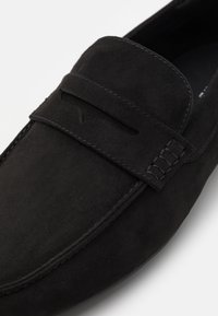 Černé semišové slip-on boty s plochým siluetou, dekorativními prošívanými detaily a výřezem v horní části poblíž špičky.