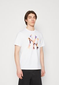 Camiseta de algodón blanca con un diseño gráfico abstracto colorido en el frontal. Mangas cortas, cuello redondo, corte relajado. Pantalones negros.