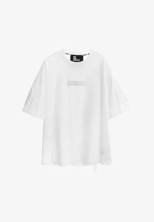 Camiseta blanca oversize de manga corta con cuello redondo, con sutiles diseños de alas bordadas en las mangas y un pequeño parche rectangular en el pecho.