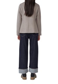 Veste en laine grise mélangée avec des épaules structurées, associée à un jean bleu foncé à jambes larges avec des ourlets roulés et des bottines noires.
