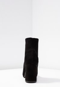 Bottes noires en suède jusqu'à la cheville avec un bout arrondi et un talon large. Comprend des détails de couture et une texture lisse.
