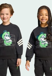 Čierna mikina s grafikou zeleného Mickey Mouse, biele prúžky na rukávoch, v kombinácii s čiernymi nohavicami. Vyrobené z mäkkého materiálu.