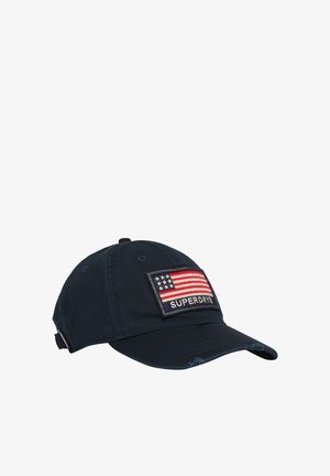 Gorra de béisbol azul marino hecha de algodón, con un parche bordado de la bandera americana y el texto "SUPERDRY" debajo. Detalles desgastados en el visor.