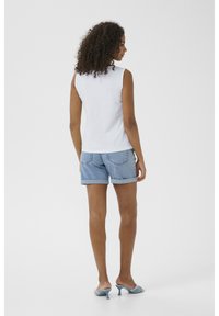 Top tanpa lengan berwarna putih dipadukan dengan celana pendek denim biru muda. Celana pendek memiliki tepi yang digulung dan saku belakang. Sepatu yang dikenakan adalah mule hak tinggi berwarna biru.