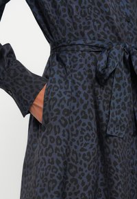 Rochie cu imprimeu de leopard în nuanțe de albastru închis și negru, cu talie legată, mâneci lungi și buzunare pe lateral. Textură netedă și moale, închidere cu butoni.