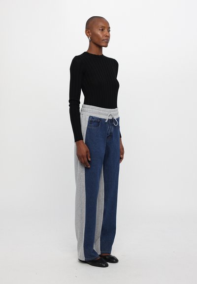 Top de manga larga de canalé negro combinado con pantalones de pierna ancha que presentan un diseño de bloques de color gris y azul. Los pantalones tienen una cintura elástica.