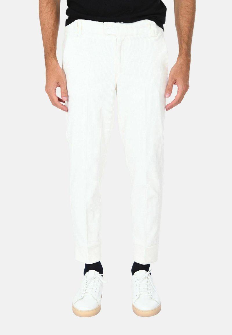 Pantaloni di velluto a coste bianchi con gamba affusolata, dotati di tasche laterali e frontale piatto, abbinati a sneakers bianche e calze blu navy.