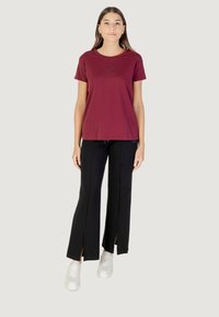 T-shirt in cotone bordeaux con maniche corte e una piccola grafica. Abbinato a pantaloni larghi neri con spacchi laterali e sneakers bianche.