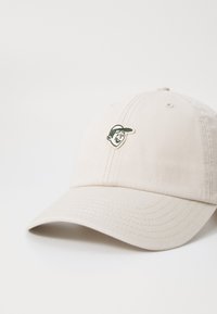 Beige cotton baseball cap with a slightly curved brim, featuring a green embroidered logo of a character on the front.