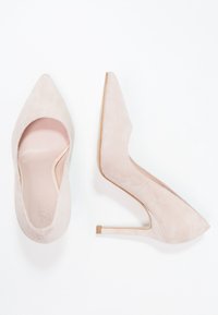 Ljusrosa mockahögklackade skor med spetsig tå, ett utskärningsdesign och en smal stilettklack med en rektangulär metallackcent.