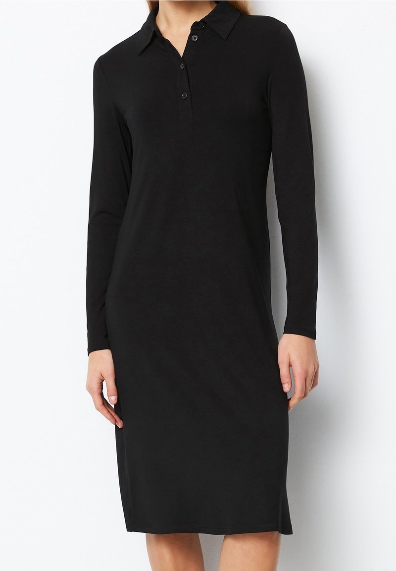 Svart långärmad poloklänning i mjukt tyg, med en krage som knäpps med knappar och en stilren, rak siluett. Inga synliga mönster eller detaljer.