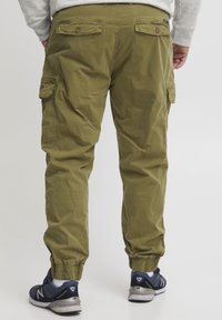 Grüne Cargo-Hosen mit elastischen Bündchen, zwei seitlichen Taschen und zwei Rückentaschen mit Klappen, kombiniert mit marineblauen Sportschuhen.