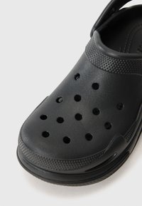 Black clog made of textured plastic, featuring ventilation holes, a defined heel, and a curved strap for a secure fit.