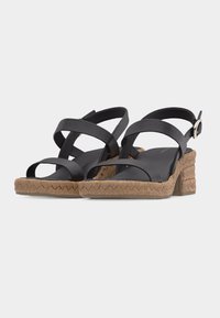 Sandales noires à brides avec talons blocs tissés couleur camel et brides à boucle à la cheville sur fond blanc.