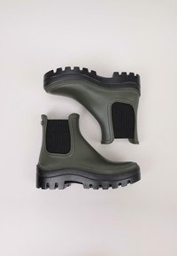 Botas de goma verde oliva hasta el tobillo con paneles laterales de elastano negro y suelas texturizadas que presentan profundas protuberancias para mayor tracción.