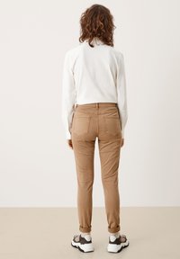 Beige Slim-Fit-Hosen mit Gesäßtaschen, kombiniert mit einem weißen Langarmhemd. Das Model trägt klobige weiß-braune Sneaker.