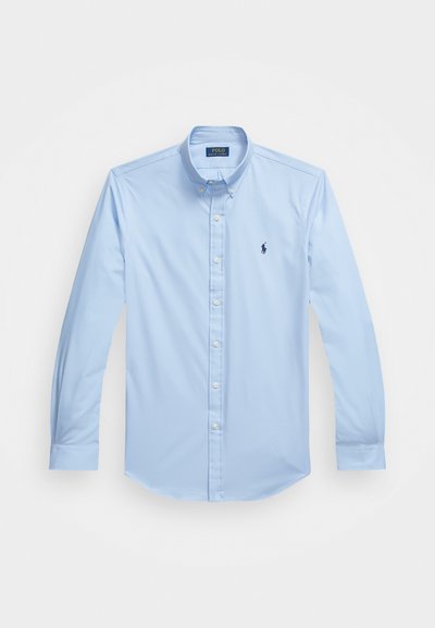 Lyseblå skjorte med knapper laget av bomull, med lange ermer, spiss krage og brodert logo på venstre bryst. Flat frontdesign.