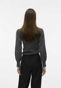 Grauer Pullover mit puffierten langen Ärmeln, körperbetontem Schnitt und gerippten Bündchen, kombiniert mit hochgeschnittenen schwarzen Hosen.