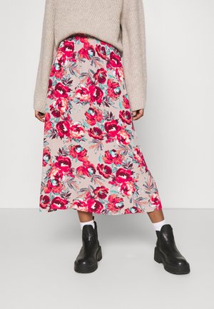 Jupe midi beige à fleurs avec des fleurs rouges et roses, assortie à des bottines noires chunky et des chaussettes blanches, portée avec un pull en tricot beige.