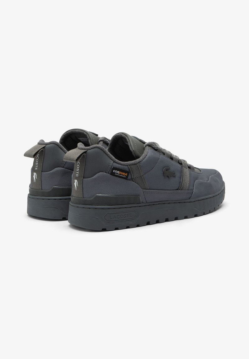 Paire de baskets Lacoste gris foncé avec semelles épaisses, dessus en tissu et languettes de tirage marquées, vues de trois quarts arrière.