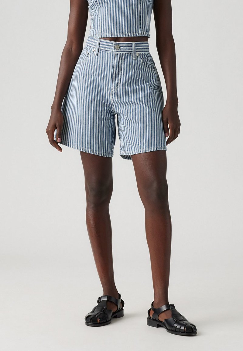 Blå och vita vertikala randiga högmidjade shorts med knappstängning och bältesöglor, tillverkade av denim. Svarta sandaletter med remmar kompletterar outfiten.