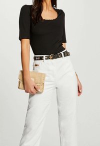 Czarna prążkowana bluzka z krótkimi rękawami, białe szerokie spodnie dżinsowe, czarny pasek ze złotymi akcentami i frędzlowy straw clutch.