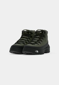 Green waterproof hiking boots with black rubber soles, featuring sturdy laces, a padded collar, and a prominent brand logo on the side.