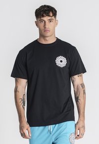 Camiseta de algodón negra con un diseño gráfico blanco en la parte izquierda del pecho. Mangas cortas y un cuello de tipo clásico.