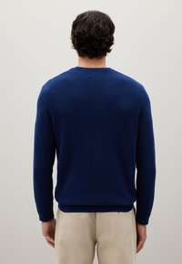 Maglione lavorato a maglia blu navy con scollatura rotonda, maniche lunghe e polsini a costine; la trama è leggermente in rilievo e strutturata.