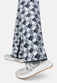 Weite Hosen in Weiß mit einem Marineblauem Kettenmuster, ausgestattet mit schwarzen Besätzen. Akzentuiert mit hellgrauen und weißen Sportschuhen.