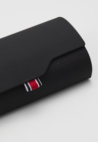 Etui pentru ochelari rectangular, negru, cu un exterior texturat, având un logo „CARRERA” embosat și un accent cu dungi roșii, albe și negre.