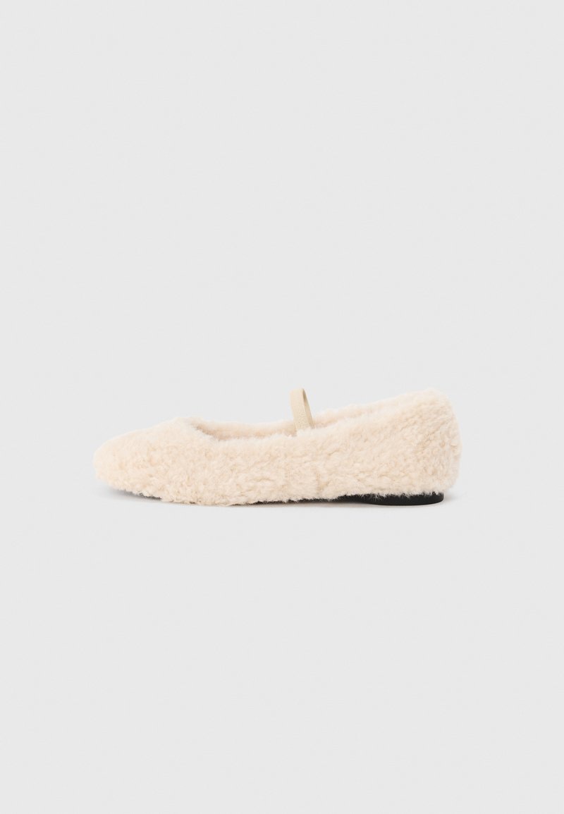 Fluffy, cream-colored slipper with a soft texture, rounded toe, minimal design, and a small fabric loop on the back for easy wear.