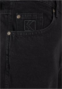 Jeans in denim nero con tasca frontale dotata di logo ricamato, bottoni metallici e un tessuto liscio e texturizzato.