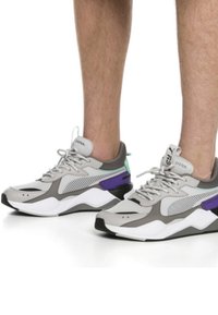 Scarpe sportive grigie con tomaia in rete, con accenti viola e verdi, un collare imbottito e una suola bianca spessa.