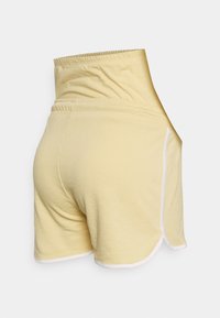 Calções de algodão amarelos com uma cintura alta, apresentando um cós elástico e avulsões brancas na bainha. O material tem uma textura suave.