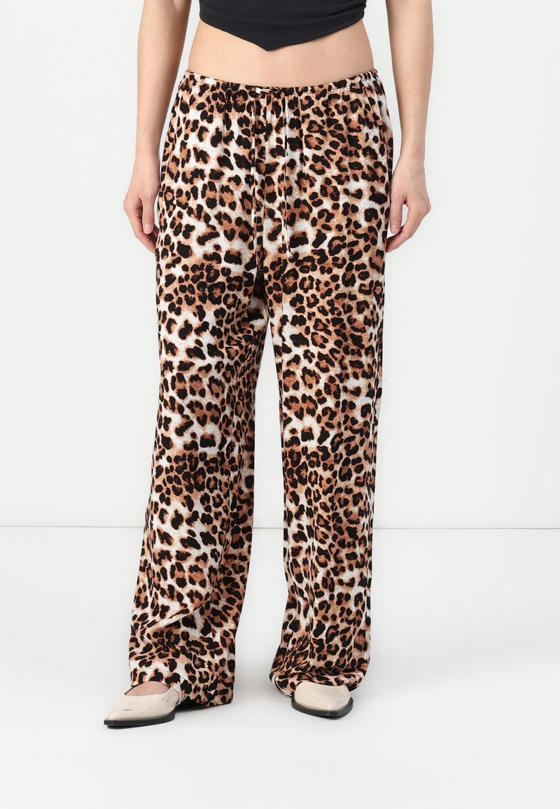 Pantalons de pyjama en imprimé léopard en tissu doux, design à jambes larges, taille mi-haute avec cordon de serrage, présentant un mélange de taches brunes, noires et blanches.