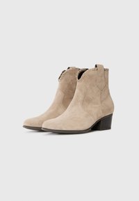 Botine din suede bej, cu guler fronsat, vârf ascuțit și toc bloc. Prezintă panouri elastice laterale pentru o îmbrăcare ușoară.