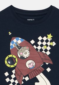 Μπλε βαμβακερό T-shirt σε ναυτικό μπλε χρώμα με σχέδιο διαστημικής πυραύλου, γεμάτο με καρτούν χαρακτήρες, κίτρινες λεπτομέρειες και στοιχεία με καρό μοτίβο.