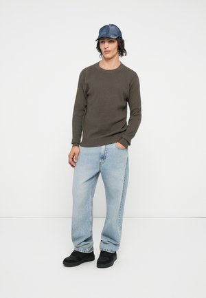 Olivengrøn ribbet sweater, lyseblå posede jeans, sorte sneakers og en blå denimkasket. Afslappet outfit med teksturerede stofdetaljer.