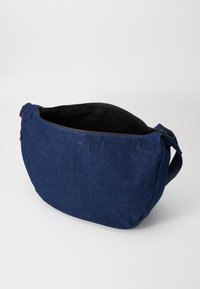 Sac à épaule en denim bleu avec une ouverture zippée, une large sangle unique et une doublure intérieure noire. Présente un petit logo près du zip.