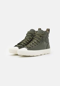 Zapatillas altas de cuero verde oliva con punta y suela de goma blanca, que presentan cordones a juego y un cuello acolchado para mayor soporte.