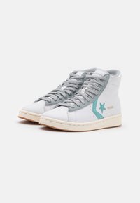 Wysokie trampki z białą skórzaną cholewką, szarymi zamszowymi akcentami, turkusowym logo w kształcie gwiazdy oraz kremową gumową podeszwą z teksturowymi detalami.